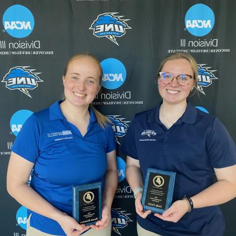 Two female students pose for a photo holding awards